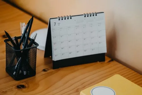 A desk calendar and a pot of pens on a wooden desk
