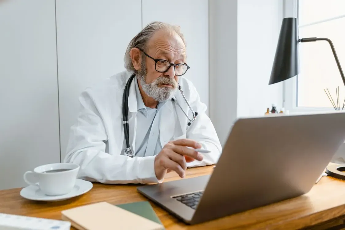 Doctor in a white coat working on a laptop at a desk in a clinic office