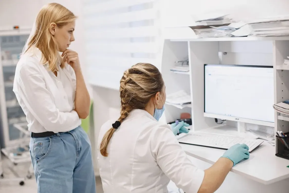 Two healthcare professionals reviewing patient records on a computer screen in a clinic